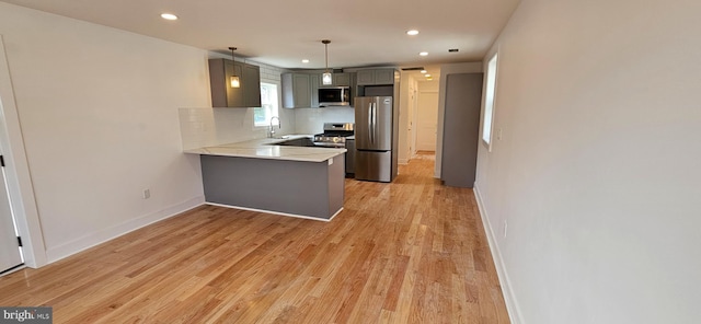 kitchen featuring backsplash, baseboards, light wood-type flooring, a peninsula, and stainless steel appliances