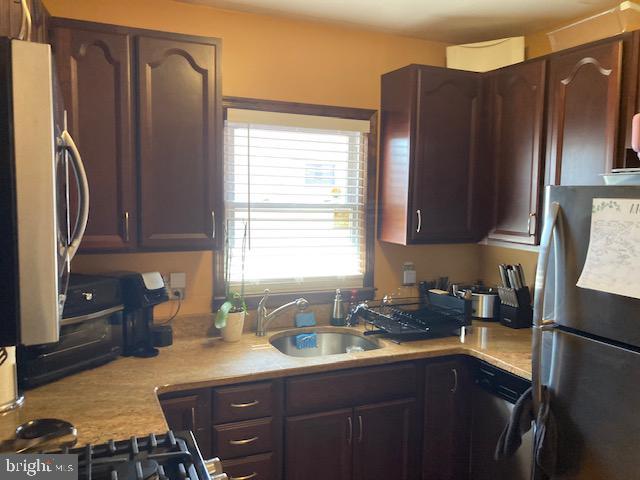 kitchen with dishwasher, light countertops, freestanding refrigerator, refrigerator, and a sink