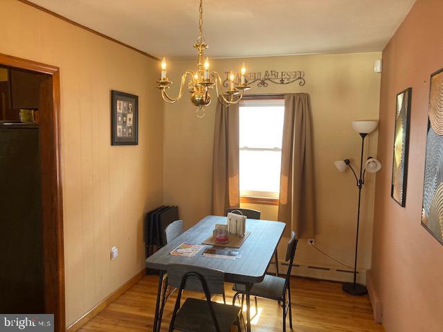 dining area featuring a baseboard radiator, baseboards, an inviting chandelier, and light wood finished floors