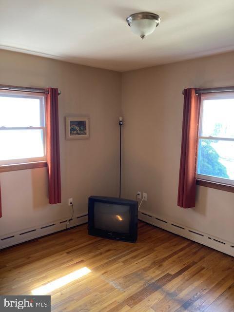 empty room featuring a baseboard radiator, a healthy amount of sunlight, and wood finished floors