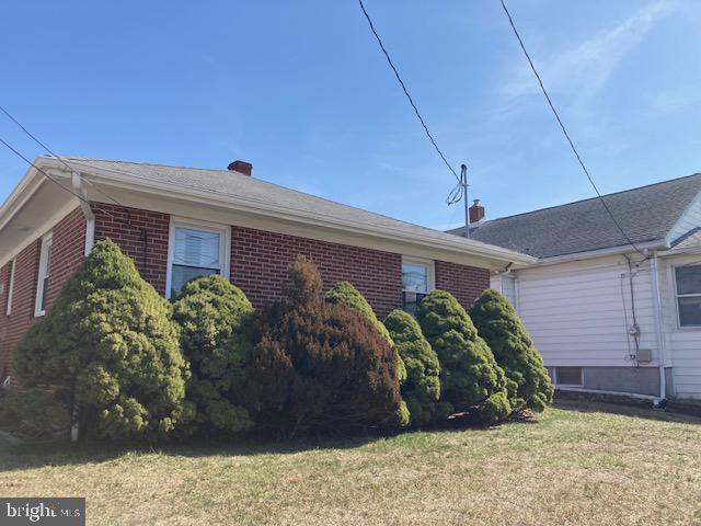 view of side of property with brick siding, a lawn, and a chimney