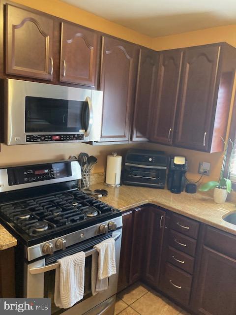 kitchen with light stone counters, light tile patterned flooring, dark brown cabinets, and stainless steel appliances