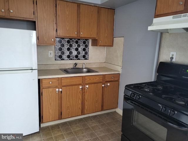 kitchen featuring black range with gas stovetop, under cabinet range hood, light countertops, freestanding refrigerator, and a sink