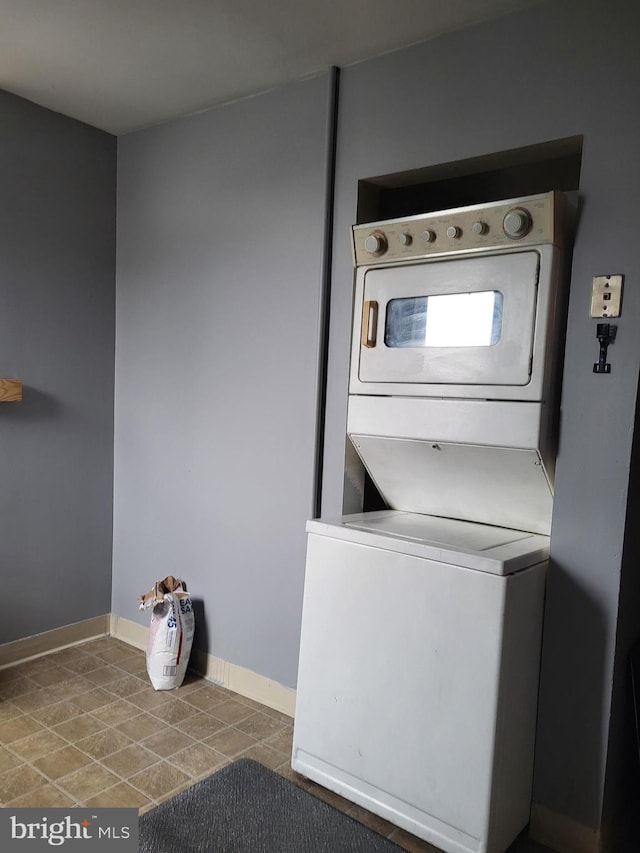 clothes washing area featuring tile patterned floors, baseboards, stacked washer and clothes dryer, and laundry area