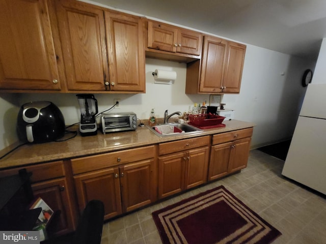 kitchen featuring a toaster, freestanding refrigerator, a sink, light countertops, and brown cabinets