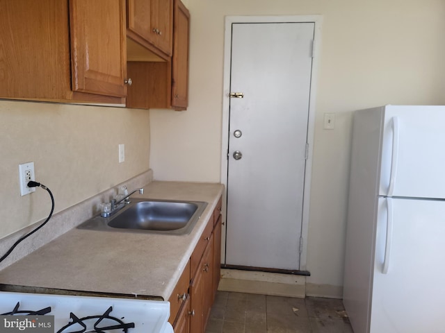 kitchen featuring a sink, freestanding refrigerator, brown cabinetry, tile patterned flooring, and light countertops