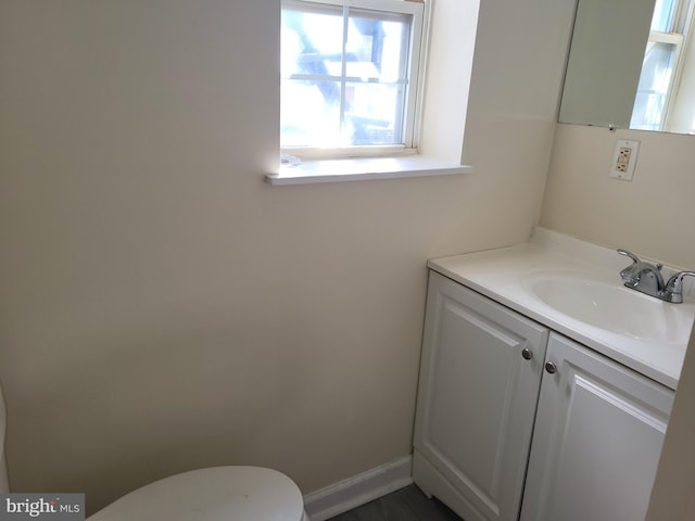 half bath with baseboards, toilet, and vanity