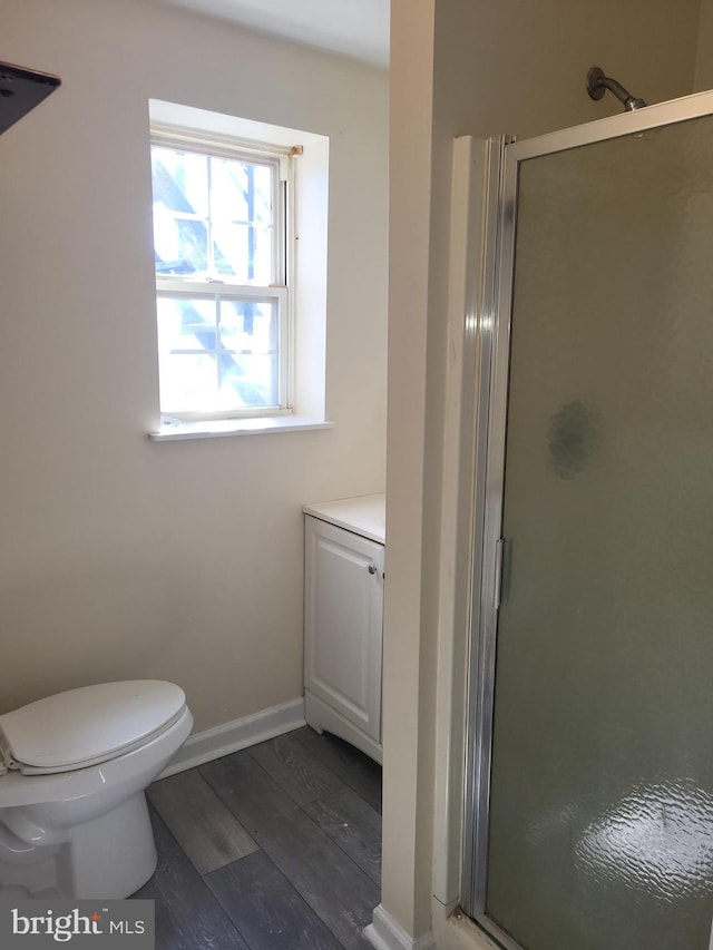 bathroom with baseboards, toilet, wood finished floors, and a shower stall