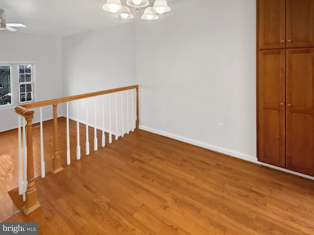 interior space featuring light wood finished floors, ceiling fan with notable chandelier, and baseboards