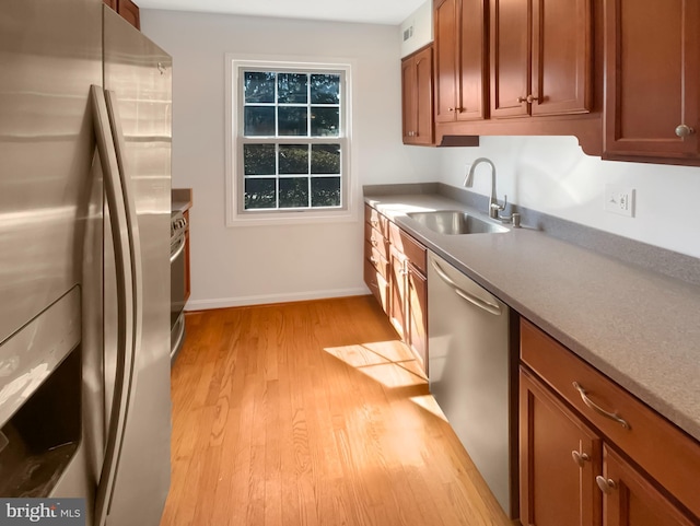 kitchen with light wood finished floors, brown cabinets, stainless steel appliances, and a sink