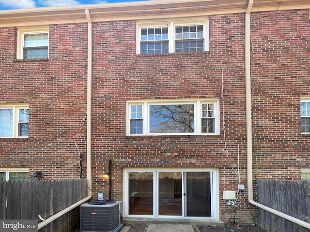 back of property with brick siding, central AC unit, and fence