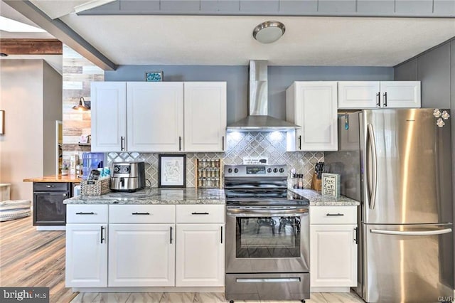 kitchen with light stone counters, backsplash, white cabinetry, appliances with stainless steel finishes, and wall chimney range hood