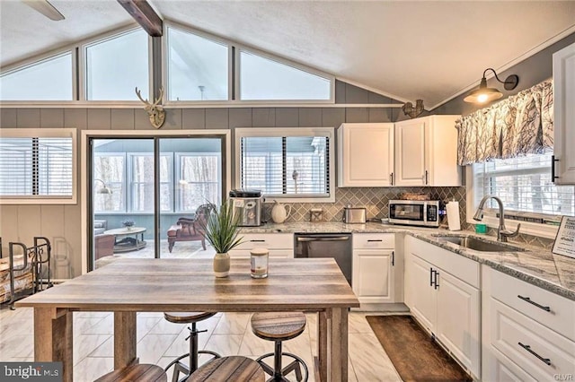 kitchen featuring vaulted ceiling with beams, light stone countertops, stainless steel appliances, white cabinetry, and a sink