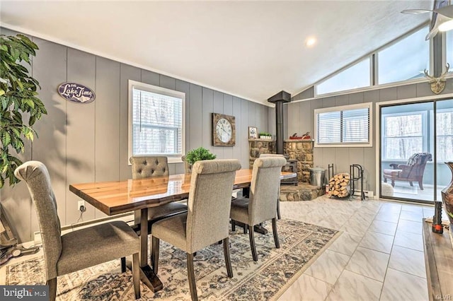 dining room featuring marble finish floor, a wood stove, and vaulted ceiling