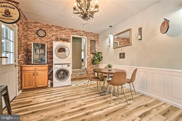 dining room featuring light wood finished floors, stacked washer / dryer, an inviting chandelier, and a wainscoted wall