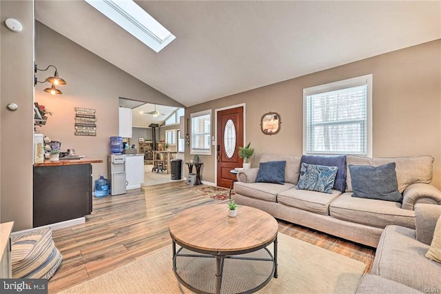 living room featuring light wood-type flooring, high vaulted ceiling, and a skylight