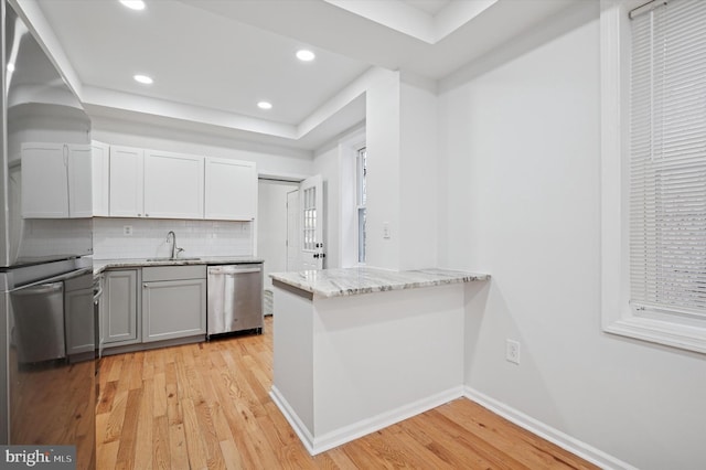 kitchen with light stone counters, light wood-style flooring, stainless steel appliances, and a sink