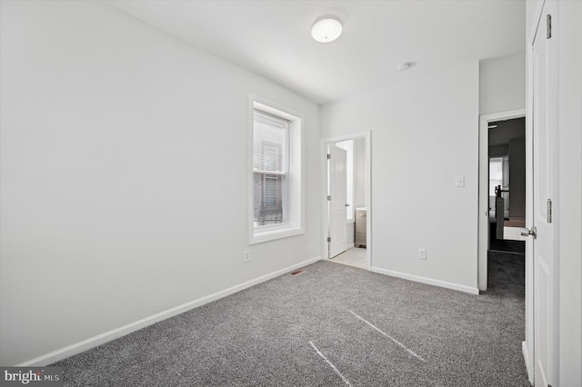 unfurnished bedroom featuring baseboards, ensuite bathroom, and carpet