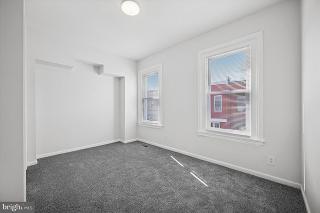 unfurnished room with baseboards and dark carpet