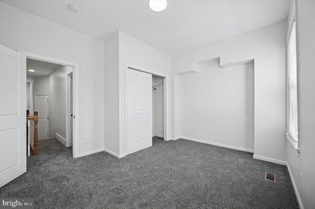 unfurnished bedroom with dark colored carpet, visible vents, baseboards, and a closet