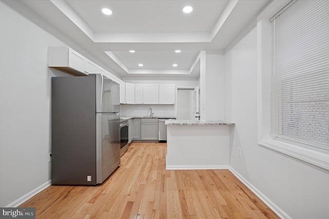 kitchen featuring a tray ceiling, light wood finished floors, baseboards, and appliances with stainless steel finishes