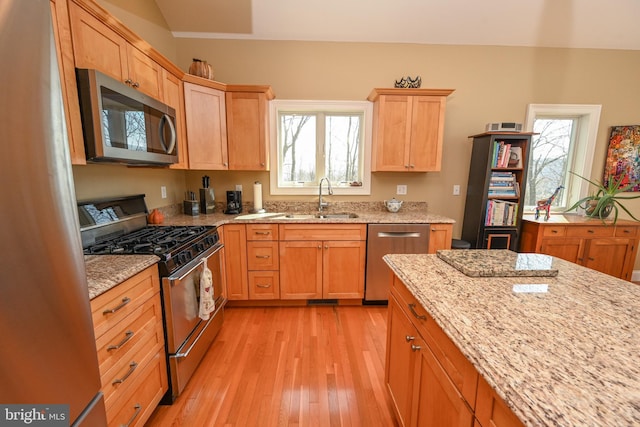 kitchen with light stone counters, light brown cabinets, light wood finished floors, a sink, and appliances with stainless steel finishes