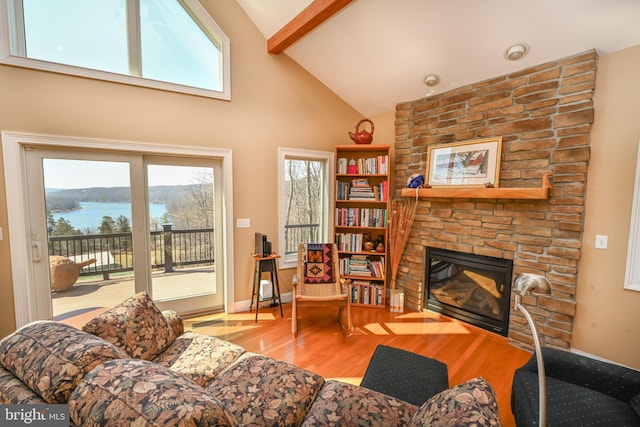 living area featuring beam ceiling, high vaulted ceiling, a water view, wood finished floors, and a stone fireplace