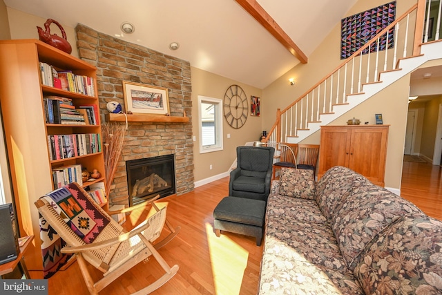 living area featuring wood finished floors, stairway, a stone fireplace, baseboards, and vaulted ceiling with beams