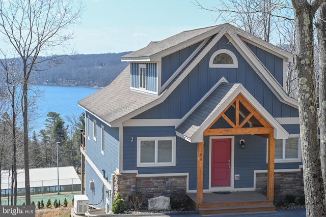 view of front facade with a water view, board and batten siding, stone siding, and roof with shingles