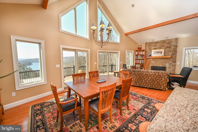 dining area with light wood-style floors, a notable chandelier, a stone fireplace, and a healthy amount of sunlight