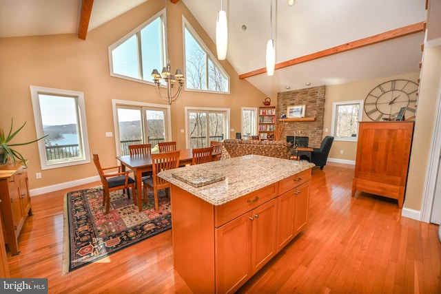 kitchen featuring beamed ceiling, light stone counters, a center island, a stone fireplace, and light wood finished floors