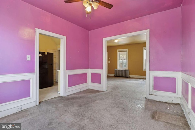 spare room with a wainscoted wall, radiator, ceiling fan, and carpet