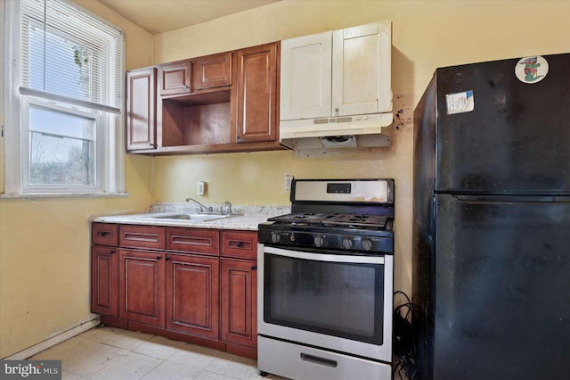 kitchen featuring a sink, under cabinet range hood, freestanding refrigerator, light countertops, and stainless steel gas range