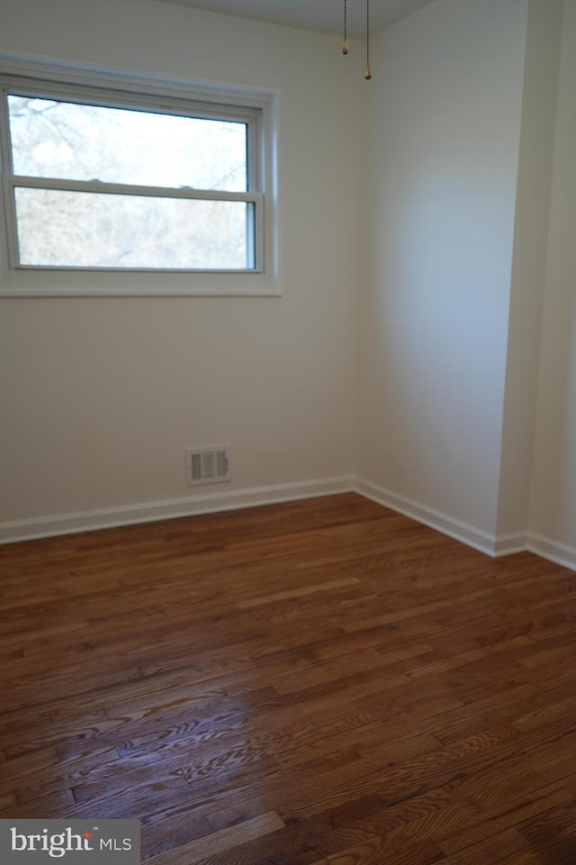 empty room with dark wood-type flooring, baseboards, and visible vents