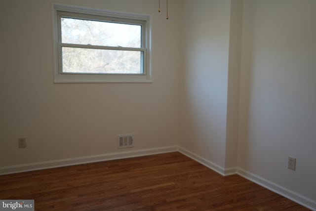 empty room featuring visible vents, dark wood-type flooring, and baseboards