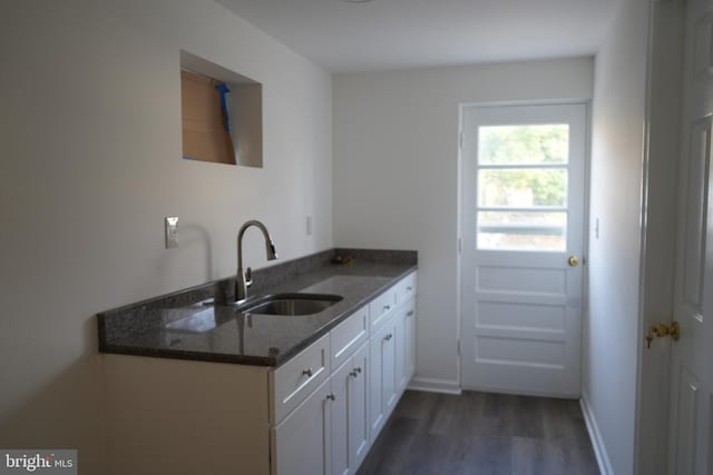 kitchen with a sink, dark stone countertops, dark wood-style floors, white cabinetry, and baseboards