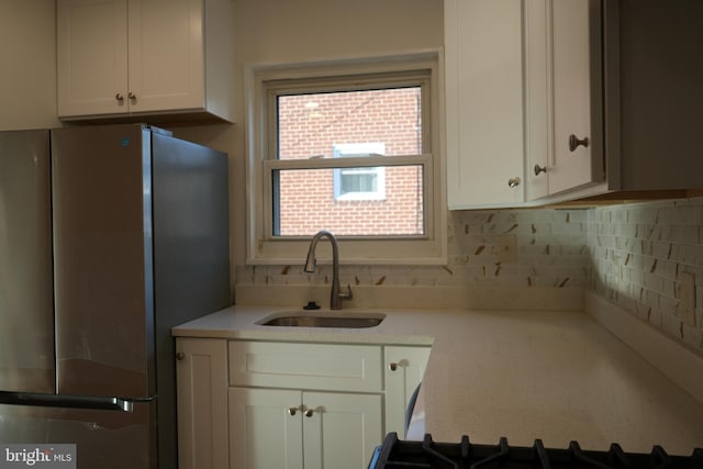 kitchen featuring a sink, backsplash, white cabinets, and freestanding refrigerator