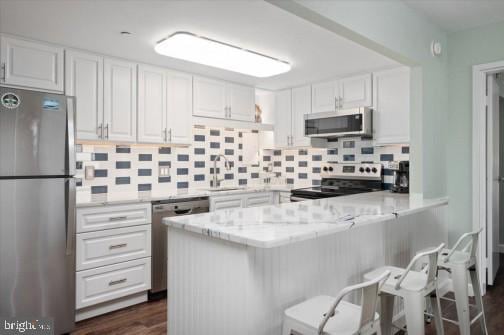 kitchen with a peninsula, a sink, white cabinets, appliances with stainless steel finishes, and backsplash