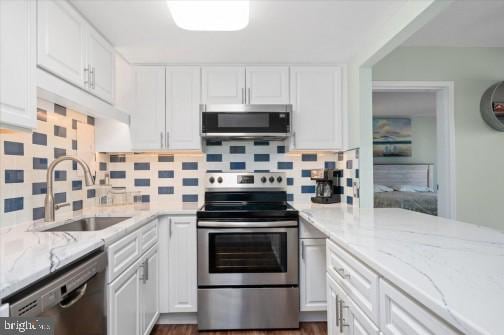 kitchen with light stone countertops, a sink, stainless steel appliances, white cabinets, and backsplash