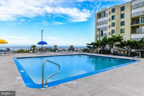 community pool featuring a water view, a patio, and fence