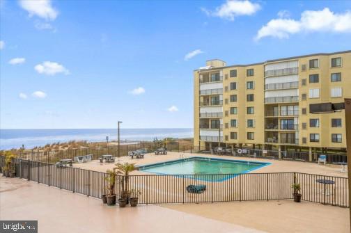 pool featuring a patio area, a water view, and fence