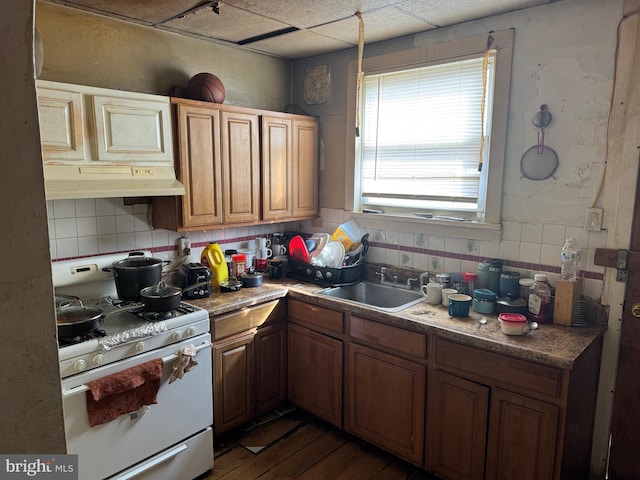 kitchen with under cabinet range hood, brown cabinets, gas range gas stove, and a sink