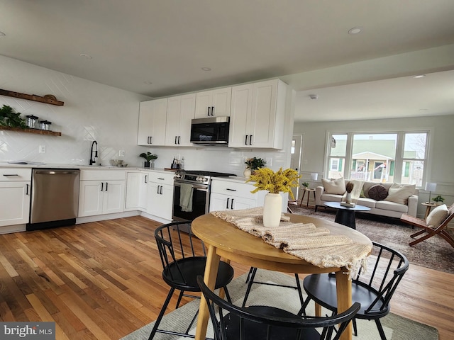 kitchen featuring stainless steel appliances, light wood-style flooring, decorative backsplash, and white cabinetry