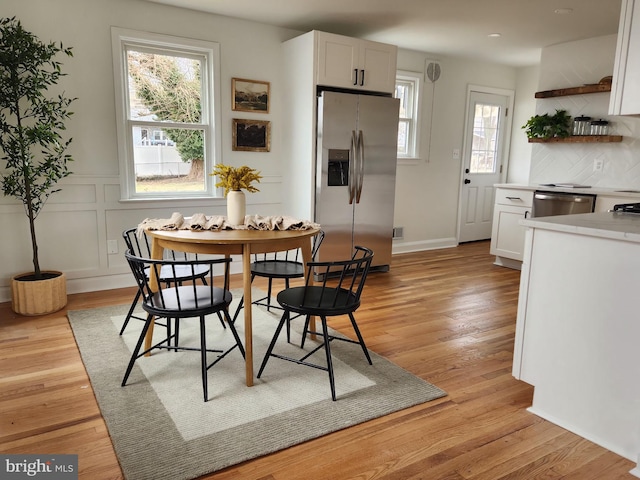 dining space with a decorative wall, wainscoting, and light wood-type flooring