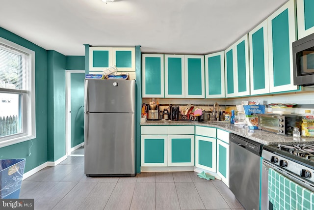 kitchen with baseboards, a toaster, light stone counters, stainless steel appliances, and a sink