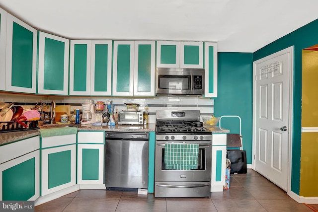 kitchen with a toaster, a sink, appliances with stainless steel finishes, dark tile patterned floors, and backsplash