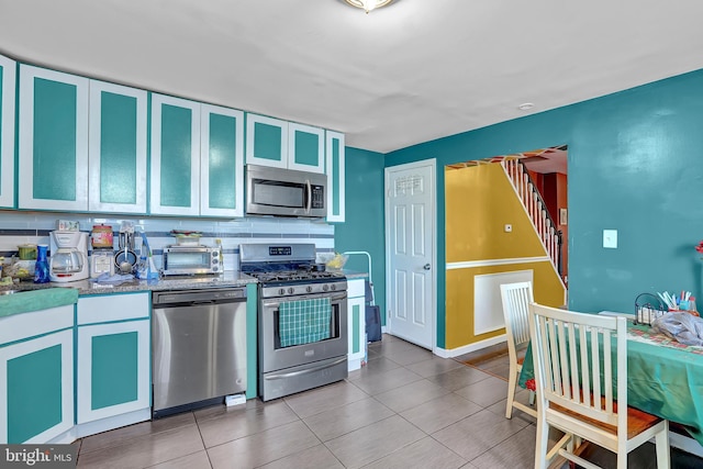 kitchen with glass insert cabinets, appliances with stainless steel finishes, tile patterned flooring, decorative backsplash, and baseboards