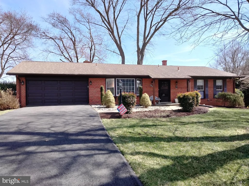 ranch-style house with aphalt driveway, an attached garage, brick siding, and a chimney