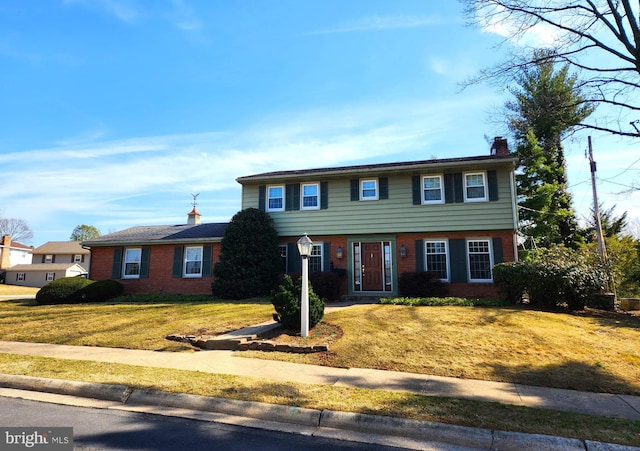 colonial home with brick siding, a chimney, and a front lawn