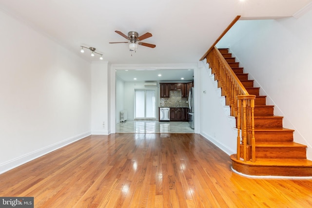 unfurnished living room featuring a ceiling fan, baseboards, radiator heating unit, stairs, and light wood-type flooring